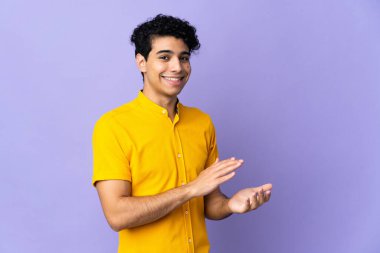 Genç Venezuelalı adam, mor arka planda izole edilmiş alkışlıyor.