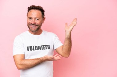 Middle age volunteer man isolated on pink background isolated on pink background extending hands to the side for inviting to come clipart