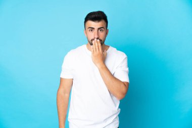 İzole edilmiş mavi arka planda, ağzı elle kaplayan beyaz bir adam.