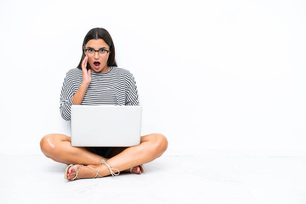 Young caucasian woman with a laptop sitting on the floor with surprise and shocked facial expression