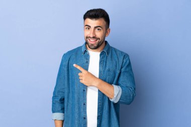 İzole edilmiş mavi arka planda beyaz bir adam bir ürünü sunmak için kenarı işaret ediyor.