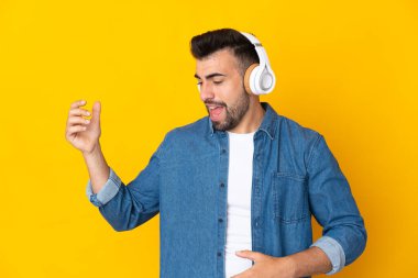 İzole edilmiş sarı arka plan üzerinde beyaz bir adam müzik dinliyor ve gitar hareketi yapıyor.