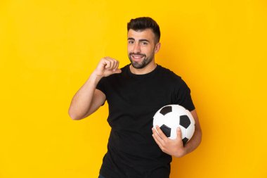Futbol topuyla izole edilmiş sarı arka planda beyaz bir adam ve kendisiyle gurur duyuyor.