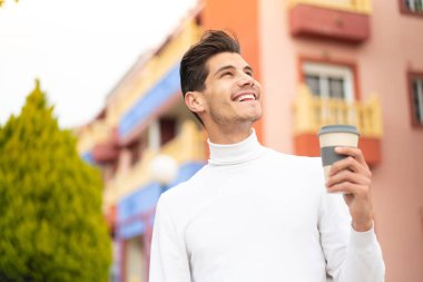 Kafkasyalı genç bir adam açık havada kahvesini yudumlarken gülümsüyor.