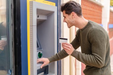 Açık havada ATM kullanan genç beyaz bir adam.