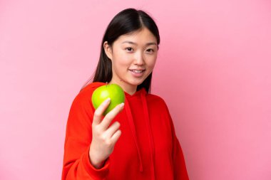 Young Chinese woman with an apple isolated on pink background with happy expression