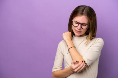 Mor arka planda, dirsek ağrısı çeken genç bir İngiliz kadın.