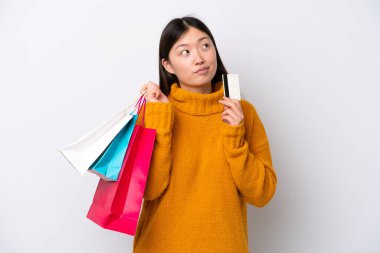 Genç Çinli bir kadın beyaz arka planda izole edilmiş. Elinde alışveriş çantaları ve bir kredi kartı var.