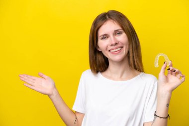 Görünmez diş tellerini tutan genç İngiliz kadın davet etmek için ellerini yana uzatıyor.