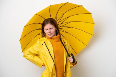 Yağmura dayanıklı ceketi ve şemsiyesi olan genç bir İngiliz kadın, beyaz arka planda, gayret gösterdiği için sırt ağrısı çekiyor.