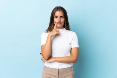 Genç Uruguaylı kadın mavi arka planda izole edilmiş ve düşünüyor