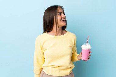 Çilekli milkshake 'li genç Uruguaylı kadın mavi arka planda izole edilmiş gülüyor.