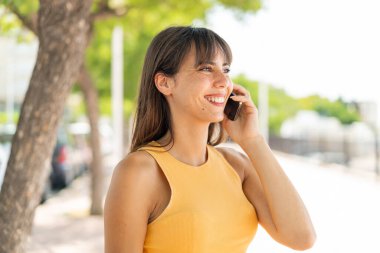 Dışarıdaki genç kadın cep telefonuyla sohbet ediyor.