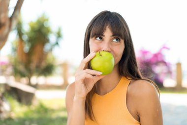 Dışarıda elinde elma tutan genç bir kadın.