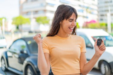 Dışarıda arabanın anahtarlarını tutan genç bir kadın zaferi kutluyor.