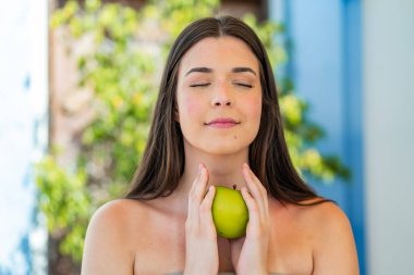 Genç, güzel Brezilyalı bir kadın açık havada elinde elma tutuyor.