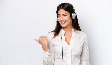 Beyaz arka planda izole edilmiş bir kulaklıkla çalışan beyaz pazarlamacı kadın bir ürünü sunmak için kenarı işaret ediyor.