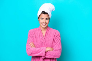 Mavi arka planda izole edilmiş bornozlu genç Brezilyalı kadın kollarını ön tarafta kavuşturuyor.