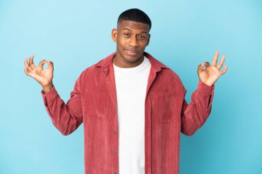 Genç latin adam Zen pozunda mavi arka planda izole.