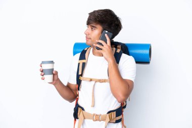İzole edilmiş beyaz arka planda büyük bir sırt çantasıyla genç dağcı kadın elinde kahve ve bir cep telefonu tutuyor.