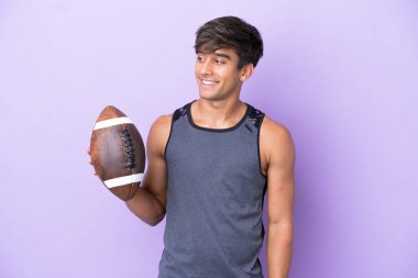 Mor arka planda izole edilmiş rugby oynayan genç adam yana bakıyor ve gülümsüyor.