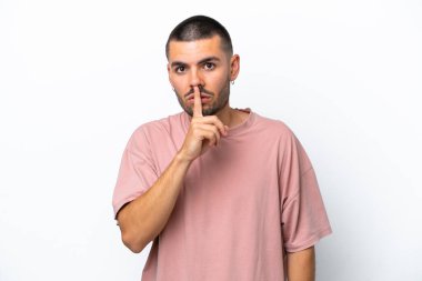 Beyaz arka planda izole edilmiş genç beyaz bir adam sessizlik işareti gösteriyor. Parmağını ağzına sokuyor.