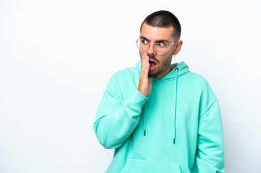 Beyaz arka planda izole edilmiş genç beyaz adam yan tarafa bakarken sürpriz bir jest yapıyor.