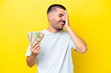 Kafkasyalı genç adam, sarı arka planda izole edilmiş bir sürü para alıyor. Çok gülümsüyor.