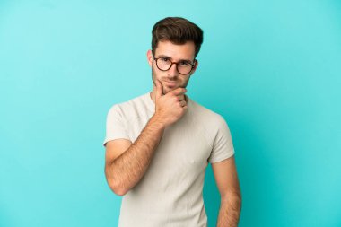 Kafkasyalı yakışıklı genç adam mavi arka planda soyutlanmış düşünüyor.