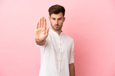 Pembe arka planda izole edilmiş beyaz, yakışıklı genç adam dur hareketi yapıyor.