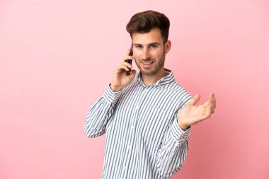 Beyaz tenli yakışıklı adam pembe arka planda izole edilmiş cep telefonuyla sohbet ediyor.