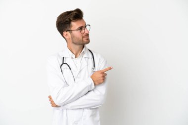 Beyaz arka planda, doktor önlüğü giymiş, beyaz tenli genç bir adam.