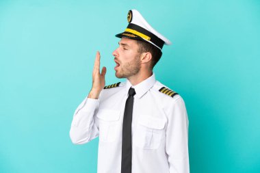 Airplane caucasian pilot isolated on blue background yawning and covering wide open mouth with hand