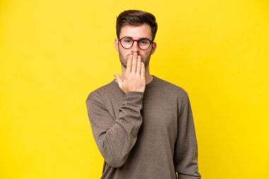 Sarı arka planda izole edilmiş, ağzı elle kaplanmış genç beyaz bir adam.