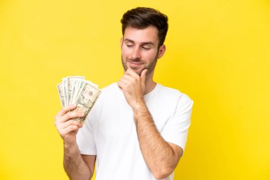 Kafkasyalı genç adam, sarı arka planda izole edilmiş bir şekilde bir sürü para alıyor. Yana bakıyor ve gülümsüyor.