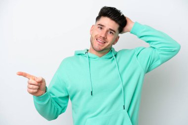 Beyaz arka planda izole edilmiş genç, beyaz bir adam şaşırmış ve parmağıyla kenarı işaret ediyor.