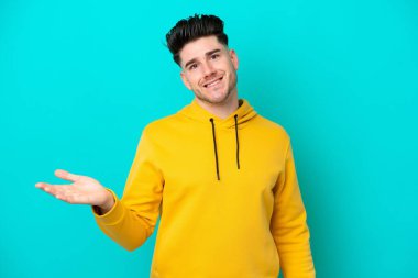 Mavi arka planda izole edilmiş genç beyaz adam gülümserken bir fikir sunuyor.