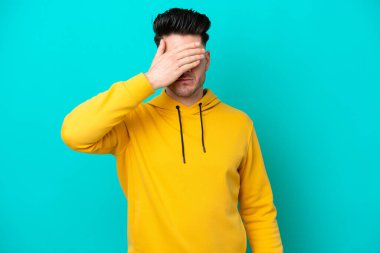 Genç beyaz adam mavi arka planda tek başına, gözleri elle kapatıyor. Bir şey görmek istemiyorum.
