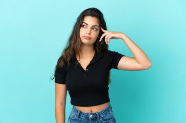 Kafkasyalı genç bir kadın mavi arka planda izole edilmiş. Delilik jesti yapıyor. Parmağını kafaya koyuyor.