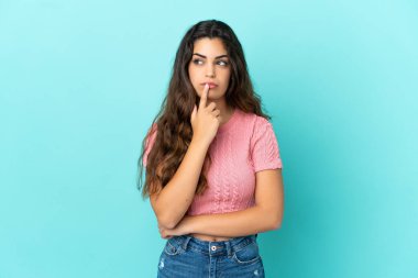 Kafkasyalı genç bir kadın mavi arka planda izole edilmiş, yukarı bakarken şüpheleri var.