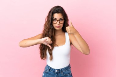 Pembe arka planda izole edilmiş beyaz bir kadın iyiye-kötüye işaret yapıyor. Evet ya da hayır arasında kararsız