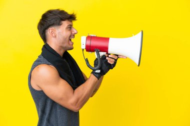 Sarı arka planda izole edilmiş havluyla genç beyaz bir adam megafondan bağırıyor.