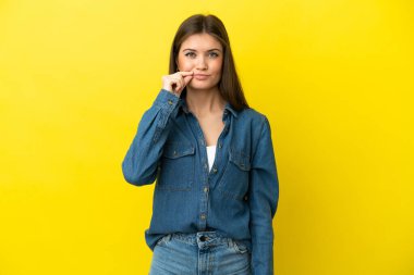 Sarı arka planda izole edilmiş genç beyaz kadın sessizlik işareti gösteriyor.