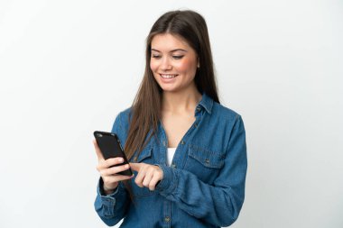 Beyaz arka planda izole edilmiş genç beyaz kadın cep telefonuyla mesaj ya da e-posta gönderiyor.