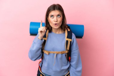 Pembe arka planda izole edilmiş büyük bir sırt çantasıyla genç dağcı kadın çözümü bulmak için parmağını kaldırıyor.