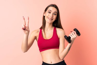 Genç sporcu kadın halter kaldırıyor izole pembe arka planda gülümsüyor ve zafer işareti gösteriyor.