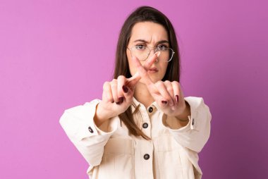 İzole edilmiş mor arka planda genç bir kadın bir eylemi durdurmak için eliyle jest yapıyor.