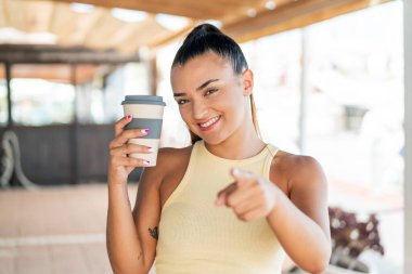 Açık havada kahve içen genç ve güzel bir kadın kendinden emin bir ifadeyle seni işaret ediyor.