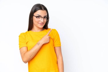 Beyaz arka planda izole edilmiş genç beyaz kadın bir ürünü sunmak için kenarı işaret ediyor.