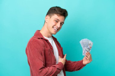 Genç Brezilyalı bir adam mavi arka planda izole edilmiş bir sürü para alıyor.